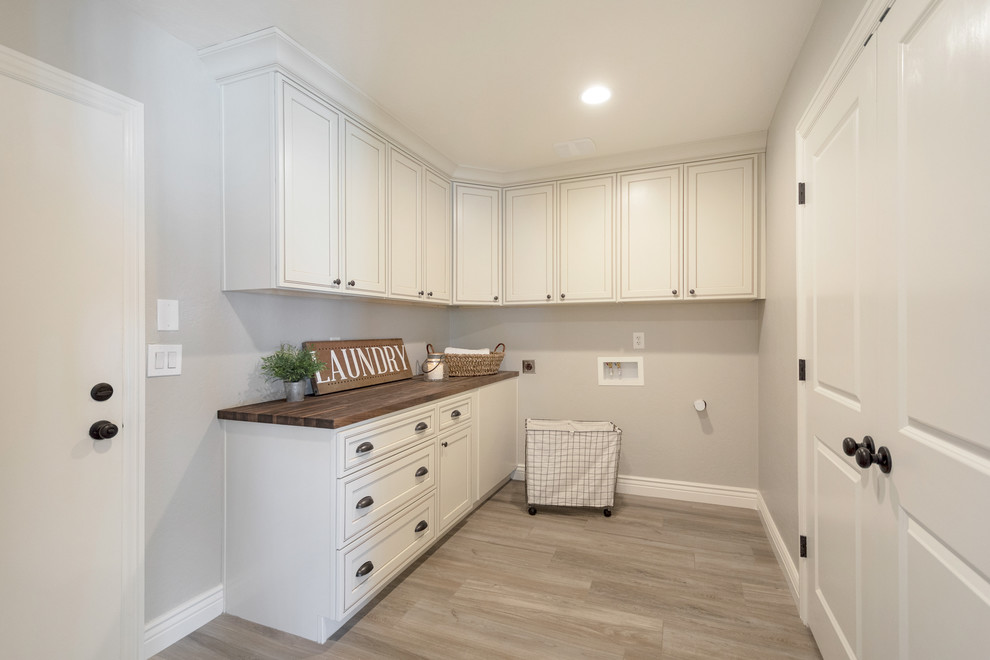 This is an example of a mid-sized country l-shaped utility room in Phoenix with recessed-panel cabinets, white cabinets, wood benchtops, grey walls, porcelain floors, a side-by-side washer and dryer, brown floor and brown benchtop.
