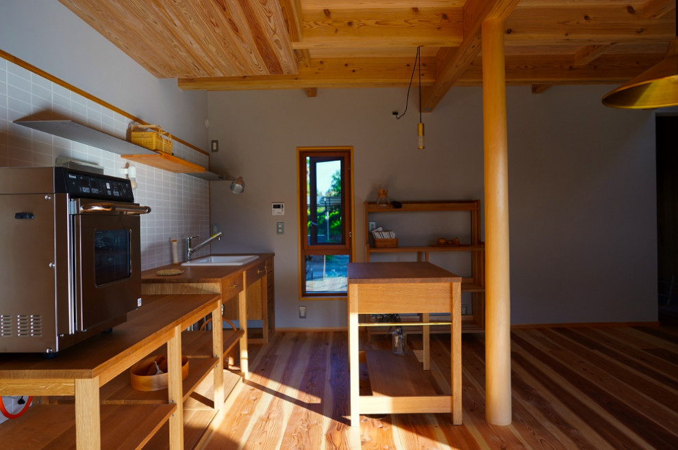 Idée de décoration pour une salle à manger ouverte sur la cuisine nordique avec un mur gris, un sol en bois brun, un poêle à bois, un manteau de cheminée en bois, un sol beige et poutres apparentes.
