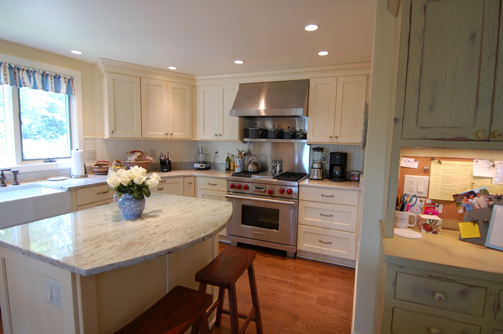 Design ideas for a mid-sized beach style kitchen in Boston with a farmhouse sink, recessed-panel cabinets, yellow cabinets, granite benchtops, white splashback, stainless steel appliances, medium hardwood floors and with island.