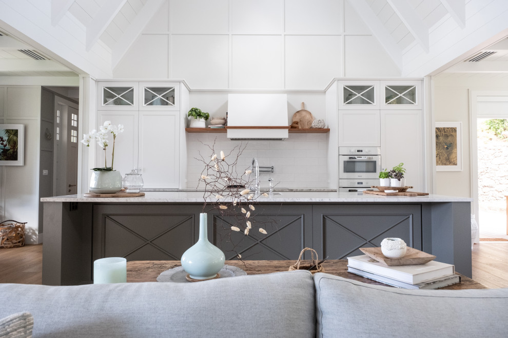 Inspiration for a transitional galley open plan kitchen in Auckland with shaker cabinets, white cabinets, white splashback, white appliances, medium hardwood floors, with island, brown floor, white benchtop and vaulted.