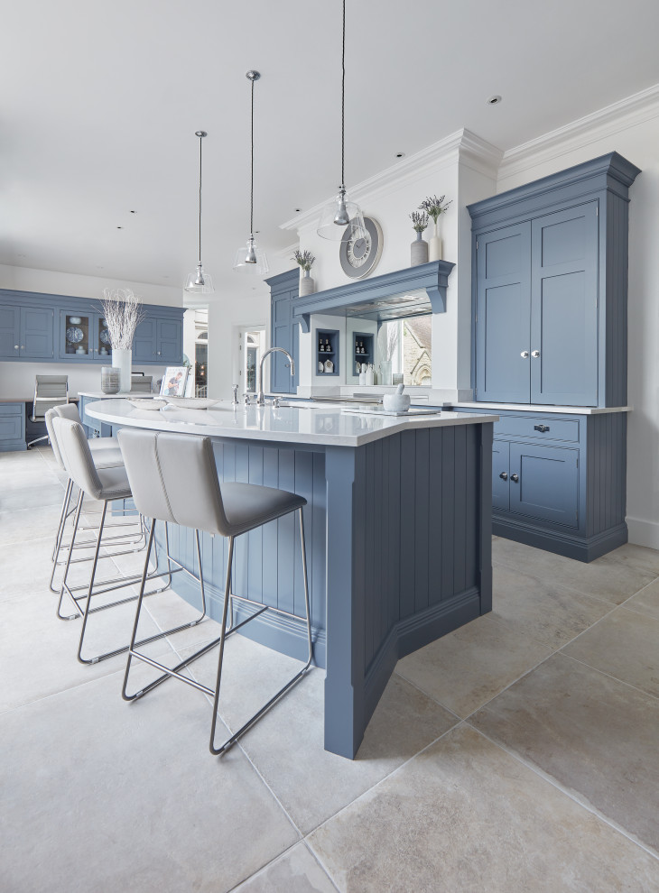 This is an example of a large traditional l-shaped kitchen in Gloucestershire with an undermount sink, shaker cabinets, blue cabinets, quartz benchtops, white splashback, mirror splashback, stainless steel appliances, limestone floors, multiple islands, beige floor and white benchtop.