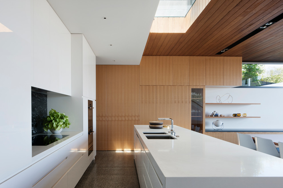 Mid-sized contemporary galley eat-in kitchen in Melbourne with white cabinets, concrete floors, with island, black splashback, stone tile splashback and an undermount sink.