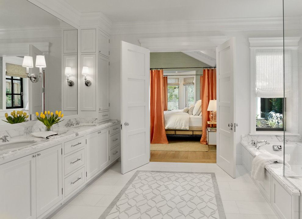 This is an example of a large traditional master bathroom in San Francisco with white cabinets, an undermount tub, white tile, white walls, marble floors, an undermount sink, marble benchtops, recessed-panel cabinets, stone slab, white floor and white benchtops.