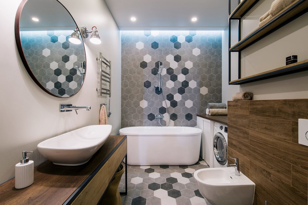 This is an example of a mid-sized contemporary master bathroom with flat-panel cabinets, brown cabinets, a freestanding tub, a shower/bathtub combo, a wall-mount toilet, gray tile, ceramic tile, grey walls, ceramic floors, a vessel sink, laminate benchtops, grey floor, an open shower and brown benchtops.