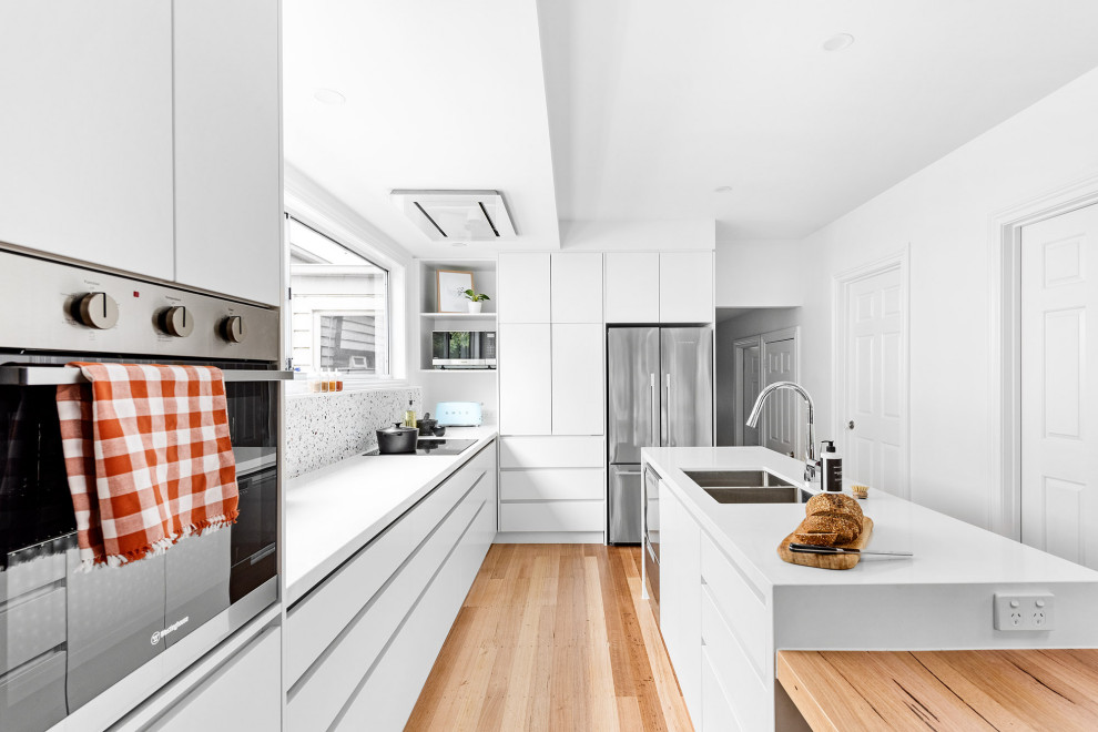 メルボルンにある高級な中くらいなモダンスタイルのおしゃれなキッチン (ダブルシンク、白いキャビネット、白いキッチンパネル、シルバーの調理設備、黄色いキッチンカウンター、三角天井) の写真