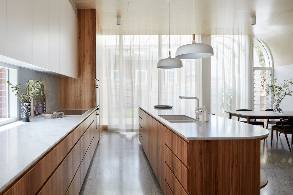 This is an example of a large contemporary l-shaped eat-in kitchen in Melbourne with a double-bowl sink, flat-panel cabinets, medium wood cabinets, marble benchtops, white splashback, marble splashback, stainless steel appliances, terrazzo floors, with island, grey floor and white benchtop.