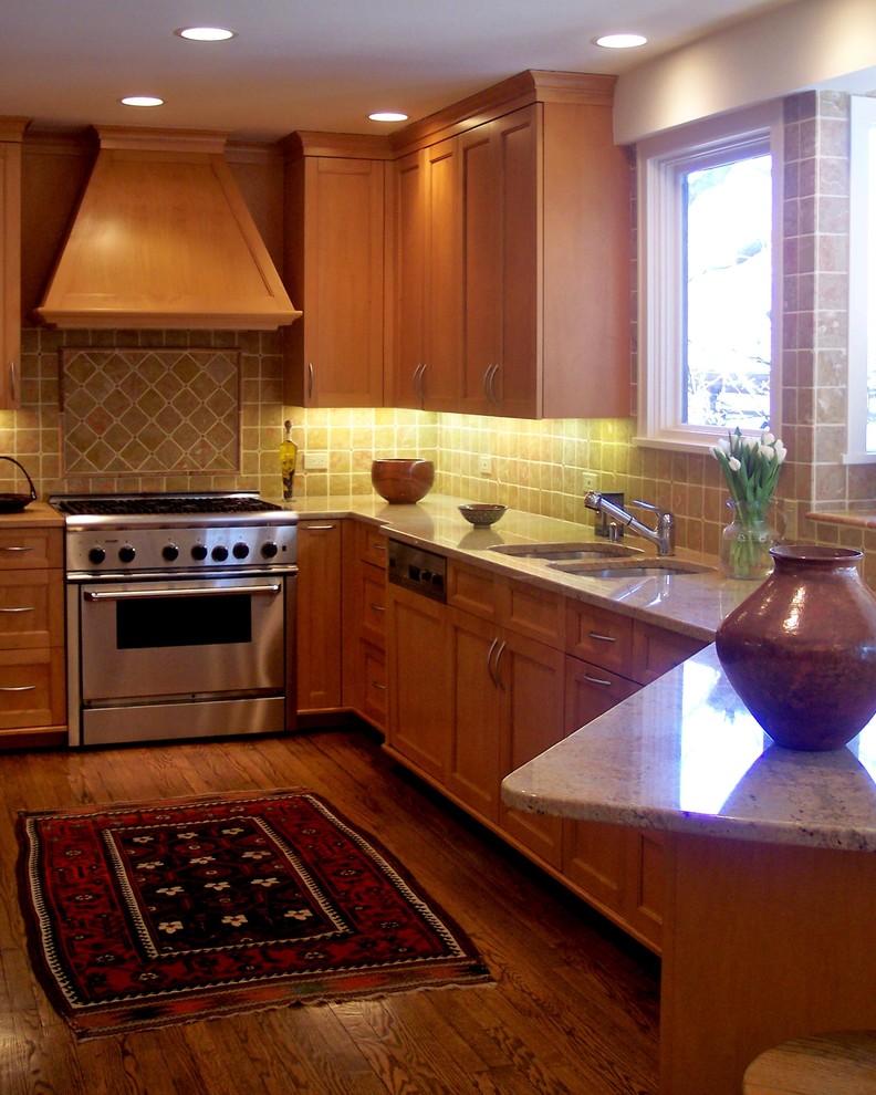 Photo of a mid-sized transitional l-shaped kitchen in Chicago with a double-bowl sink, recessed-panel cabinets, medium wood cabinets, granite benchtops, beige splashback, stone tile splashback, stainless steel appliances, dark hardwood floors, a peninsula and brown floor.