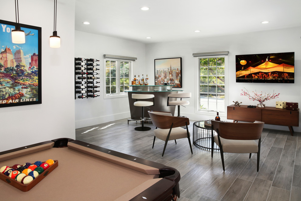 Photo of a large contemporary l-shaped seated home bar in Orange County with glass benchtops, grey floor and porcelain floors.