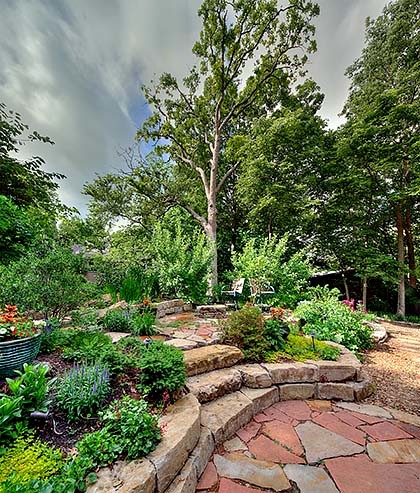 Large country backyard shaded garden in Kansas City with with privacy feature and natural stone pavers for summer.