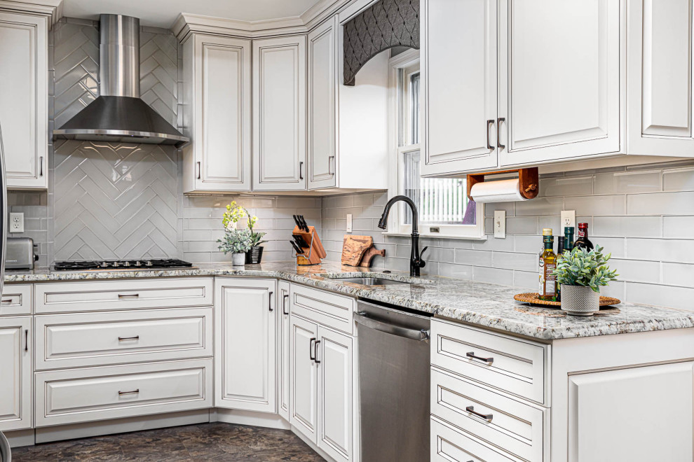 This is an example of a mid-sized l-shaped eat-in kitchen in Other with a double-bowl sink, raised-panel cabinets, white cabinets, granite benchtops, grey splashback, glass tile splashback, stainless steel appliances, ceramic floors, no island, brown floor and beige benchtop.