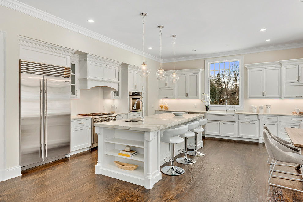Transitional l-shaped medium tone wood floor and brown floor eat-in kitchen photo in New York with a farmhouse sink, shaker cabinets, white cabinets, white backsplash, stainless steel appliances, an island and white countertops