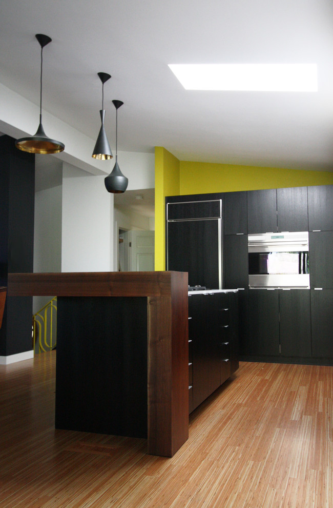 Photo of a mid-sized modern l-shaped eat-in kitchen in Portland with an undermount sink, flat-panel cabinets, black cabinets, wood benchtops, white splashback, stainless steel appliances, medium hardwood floors and with island.