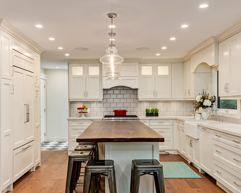 Inspiration for a mid-sized transitional l-shaped light wood floor and beige floor enclosed kitchen remodel in Calgary with a farmhouse sink, recessed-panel cabinets, white cabinets, quartz countertops, white backsplash, porcelain backsplash, stainless steel appliances and an island