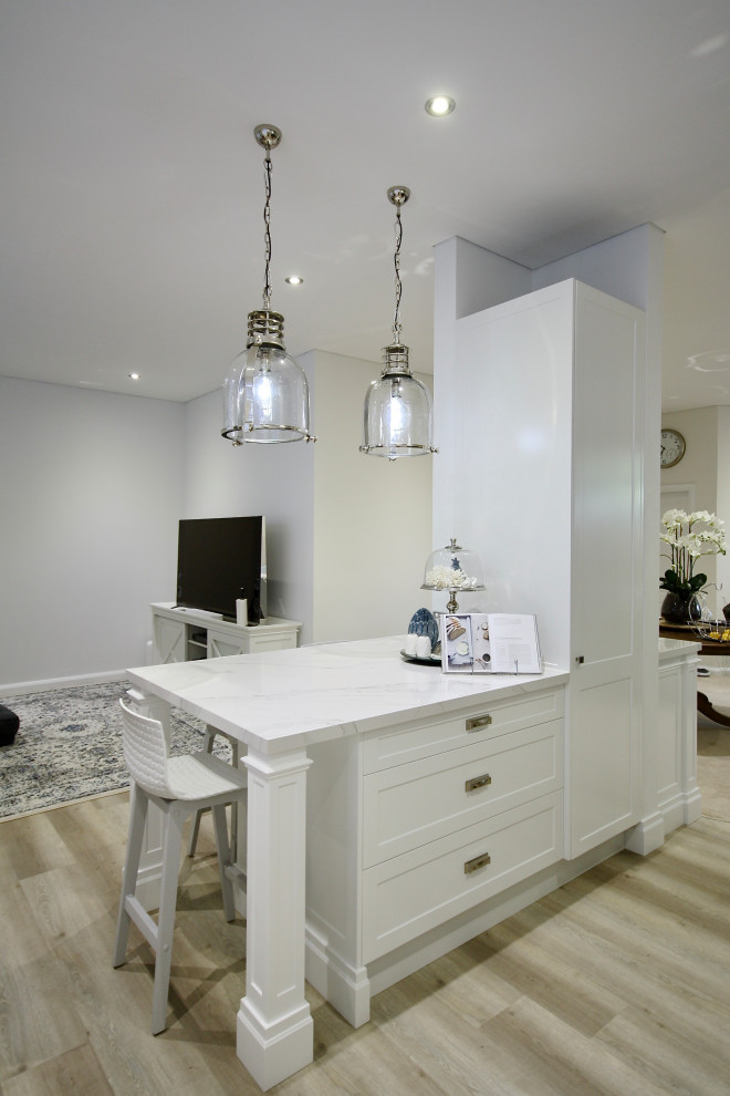 This is an example of a mid-sized transitional l-shaped open plan kitchen in Sydney with an undermount sink, shaker cabinets, white cabinets, quartz benchtops, white splashback, subway tile splashback, stainless steel appliances, light hardwood floors, with island, brown floor and white benchtop.