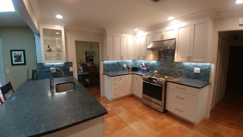 This is an example of a mid-sized transitional u-shaped eat-in kitchen in Tampa with an undermount sink, shaker cabinets, white cabinets, granite benchtops, blue splashback, mosaic tile splashback, stainless steel appliances, terra-cotta floors, a peninsula, orange floor and grey benchtop.