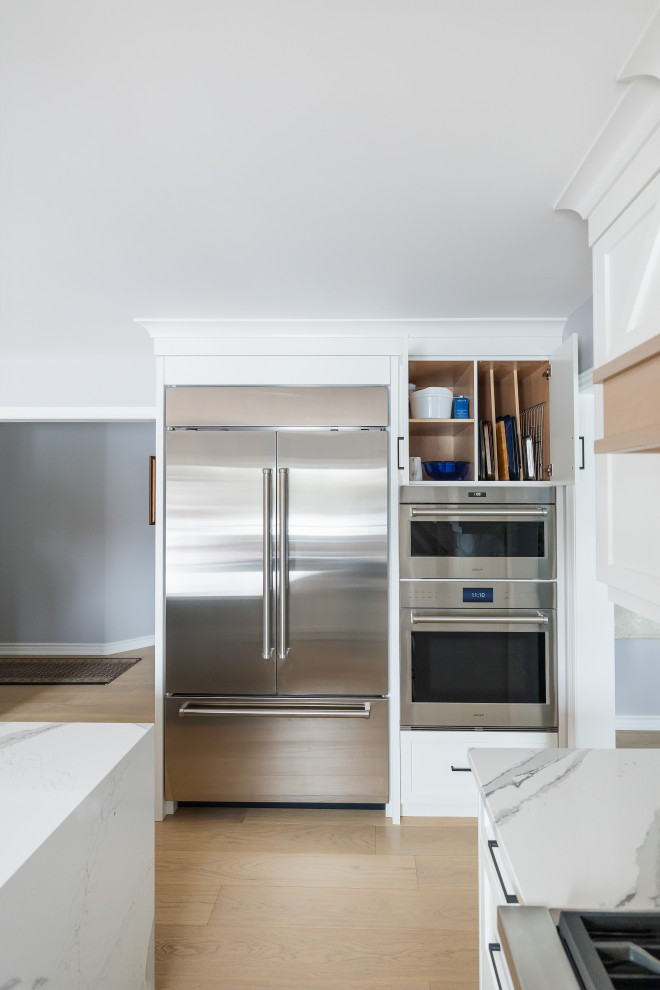 Example of a mid-sized transitional u-shaped light wood floor eat-in kitchen design in Toronto with an undermount sink, shaker cabinets, white cabinets, quartz countertops, white backsplash, quartz backsplash, stainless steel appliances, an island and white countertops