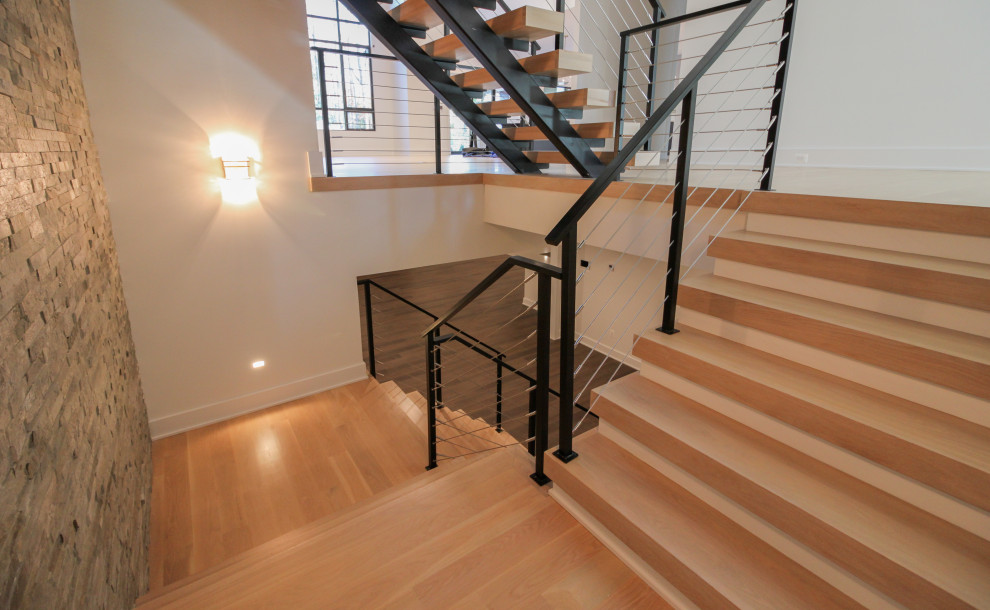 Ejemplo de escalera suspendida ecléctica grande con escalones de madera, barandilla de metal y ladrillo