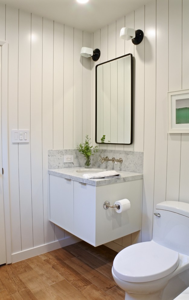 Design ideas for a small beach style bathroom in Los Angeles with flat-panel cabinets, white cabinets, an alcove tub, an alcove shower, a one-piece toilet, marble, white walls, an undermount sink, marble benchtops, brown floor, medium hardwood floors and white benchtops.