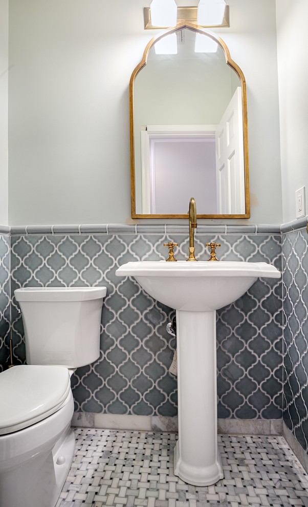 Photo of a small transitional powder room in New York with a pedestal sink, a two-piece toilet, gray tile, ceramic tile, beige walls, marble floors and white floor.
