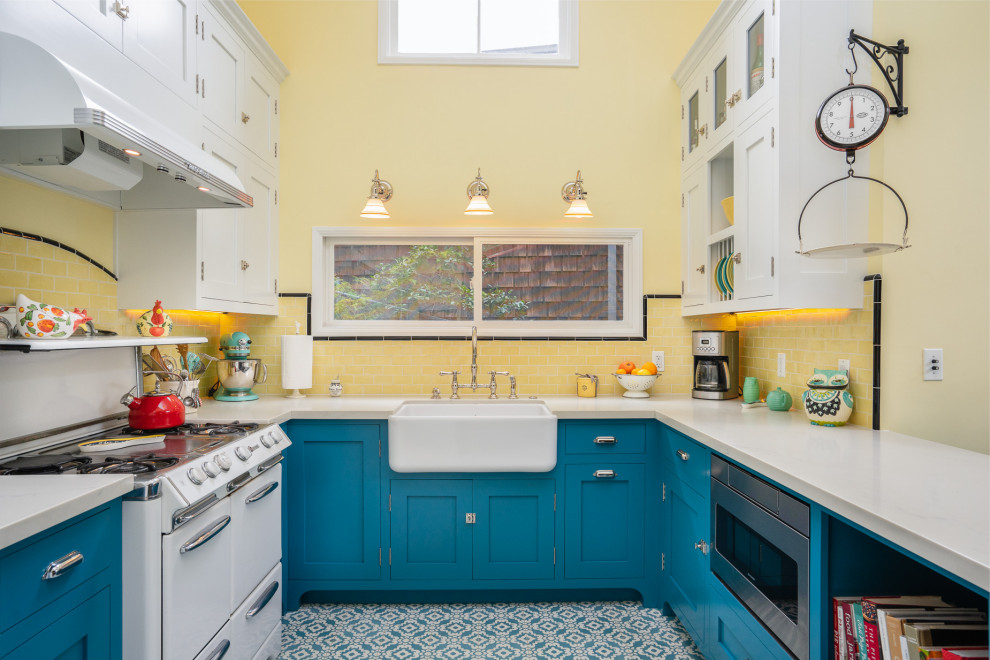 Design ideas for a mid-sized transitional u-shaped eat-in kitchen in Los Angeles with a farmhouse sink, blue cabinets, quartz benchtops, yellow splashback, subway tile splashback, white appliances, cement tiles, blue floor, white benchtop, shaker cabinets and no island.