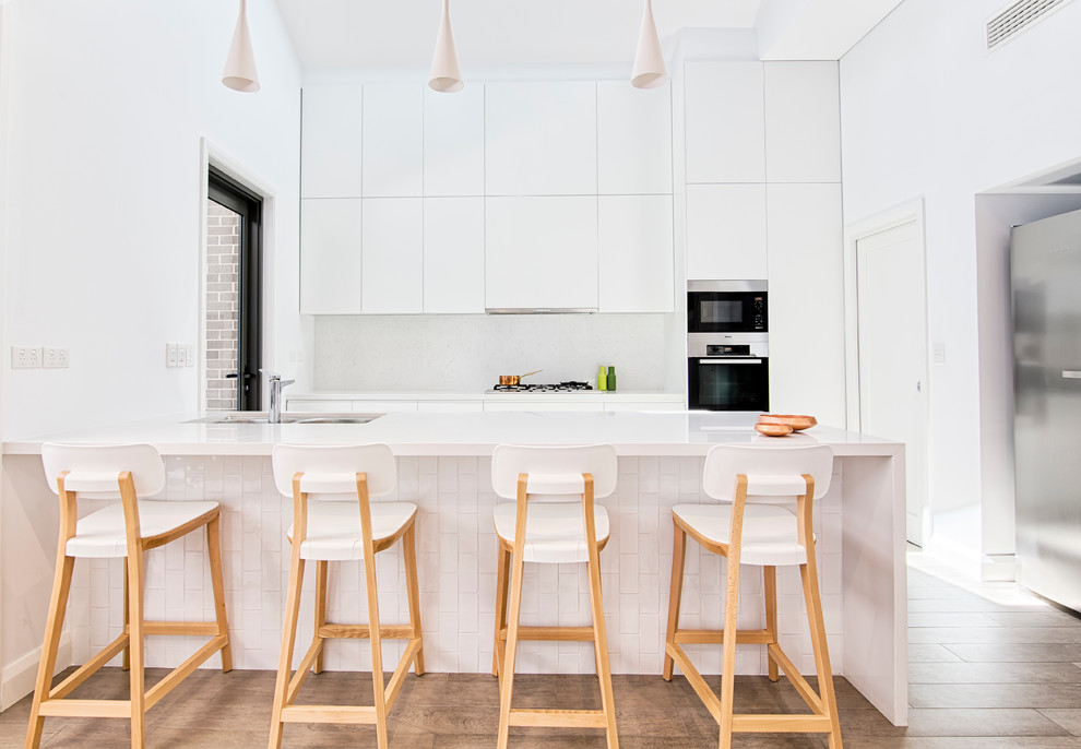 Inspiration for a large contemporary l-shaped eat-in kitchen in Sydney with a double-bowl sink, flat-panel cabinets, white cabinets, white splashback, glass sheet splashback, stainless steel appliances, light hardwood floors and with island.