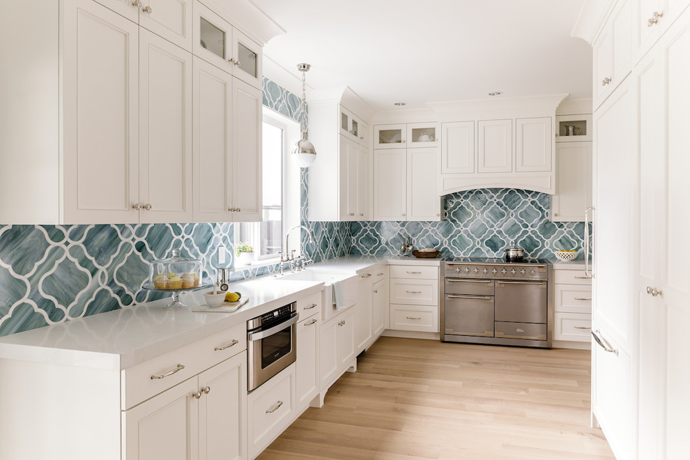 Design ideas for a mid-sized transitional u-shaped kitchen in Portland with a farmhouse sink, recessed-panel cabinets, white cabinets, quartz benchtops, panelled appliances, light hardwood floors, blue splashback and glass tile splashback.