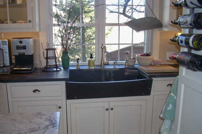 Large transitional l-shaped travertine floor and beige floor eat-in kitchen photo in Boston with a farmhouse sink, recessed-panel cabinets, white cabinets, granite countertops, white backsplash, subway tile backsplash, paneled appliances, an island and black countertops