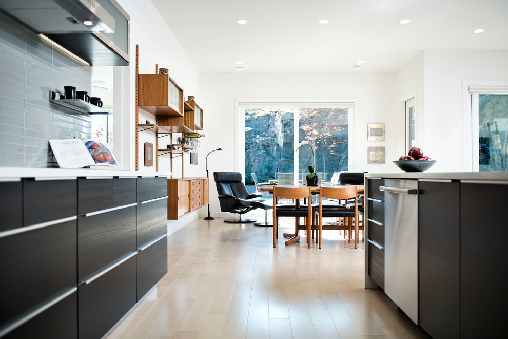 This is an example of a mid-sized contemporary l-shaped open plan kitchen in Orange County with an undermount sink, glass-front cabinets, stainless steel cabinets, solid surface benchtops, grey splashback, porcelain splashback, stainless steel appliances, light hardwood floors, with island and beige floor.