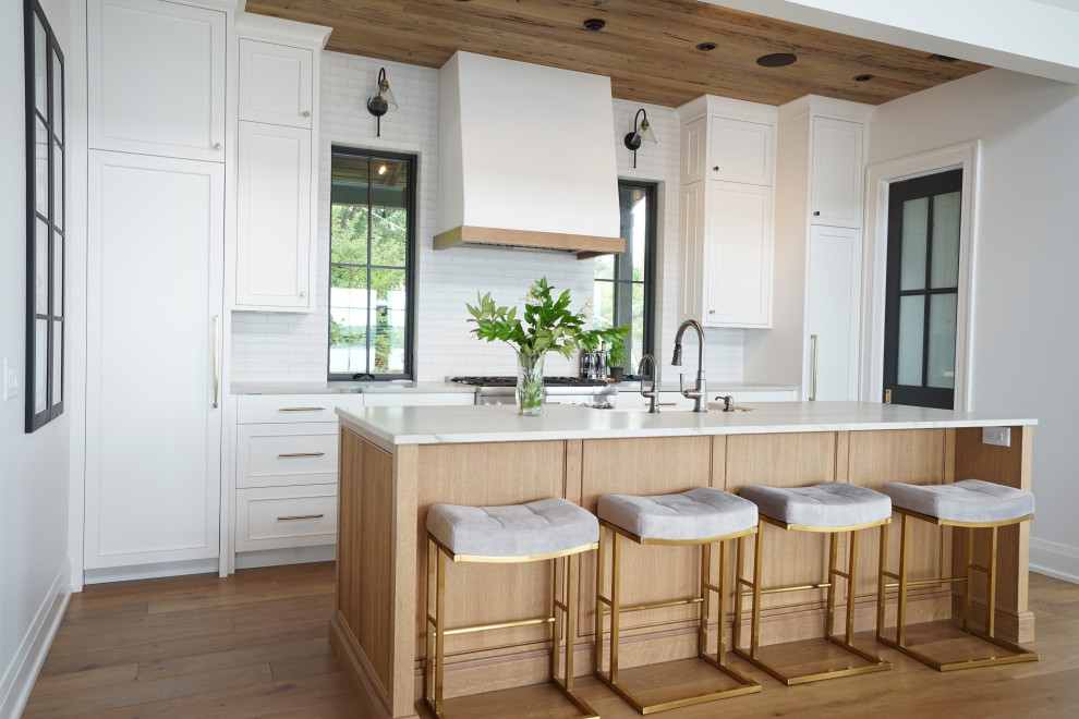 Photo of a mid-sized traditional kitchen in Other with a farmhouse sink, flat-panel cabinets, medium wood cabinets, white splashback, subway tile splashback, panelled appliances, medium hardwood floors, with island, brown floor, grey benchtop and wood.
