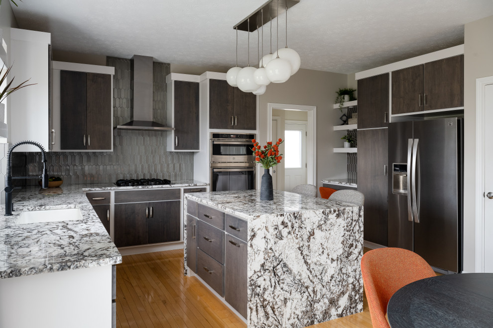 This is an example of a medium sized contemporary l-shaped kitchen/diner in Indianapolis with a submerged sink, flat-panel cabinets, brown cabinets, granite worktops, grey splashback, stainless steel appliances, medium hardwood flooring and an island.