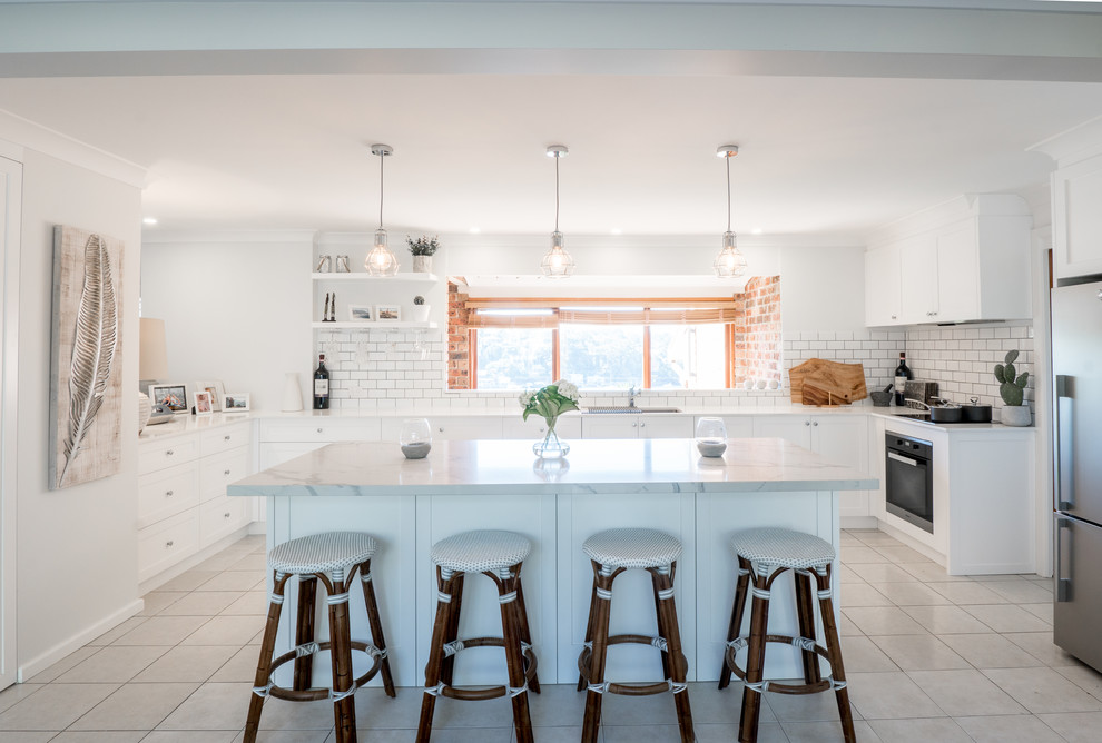 This is an example of a large contemporary u-shaped eat-in kitchen in Sydney with an undermount sink, shaker cabinets, white cabinets, quartz benchtops, white splashback, subway tile splashback, stainless steel appliances, terra-cotta floors, with island, white floor and white benchtop.
