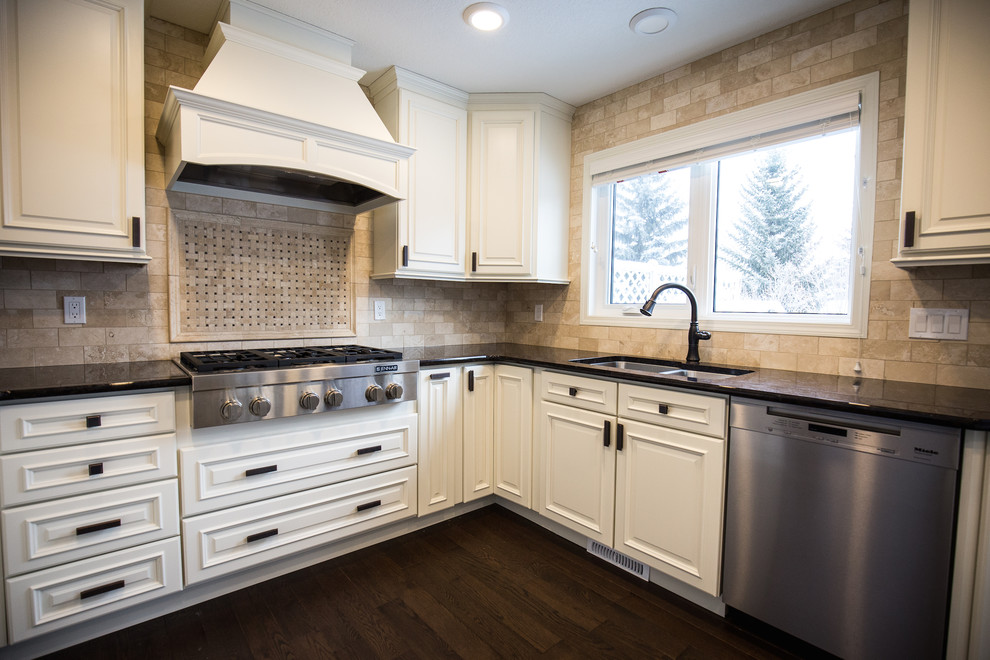 Eat-in kitchen - mid-sized traditional u-shaped dark wood floor eat-in kitchen idea in Edmonton with a drop-in sink, white cabinets, granite countertops, beige backsplash, stone tile backsplash, stainless steel appliances and an island
