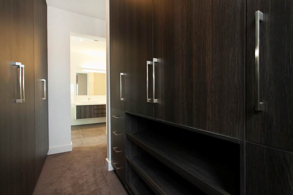 This is an example of a mid-sized contemporary gender-neutral walk-in wardrobe in Melbourne with raised-panel cabinets, dark wood cabinets and carpet.