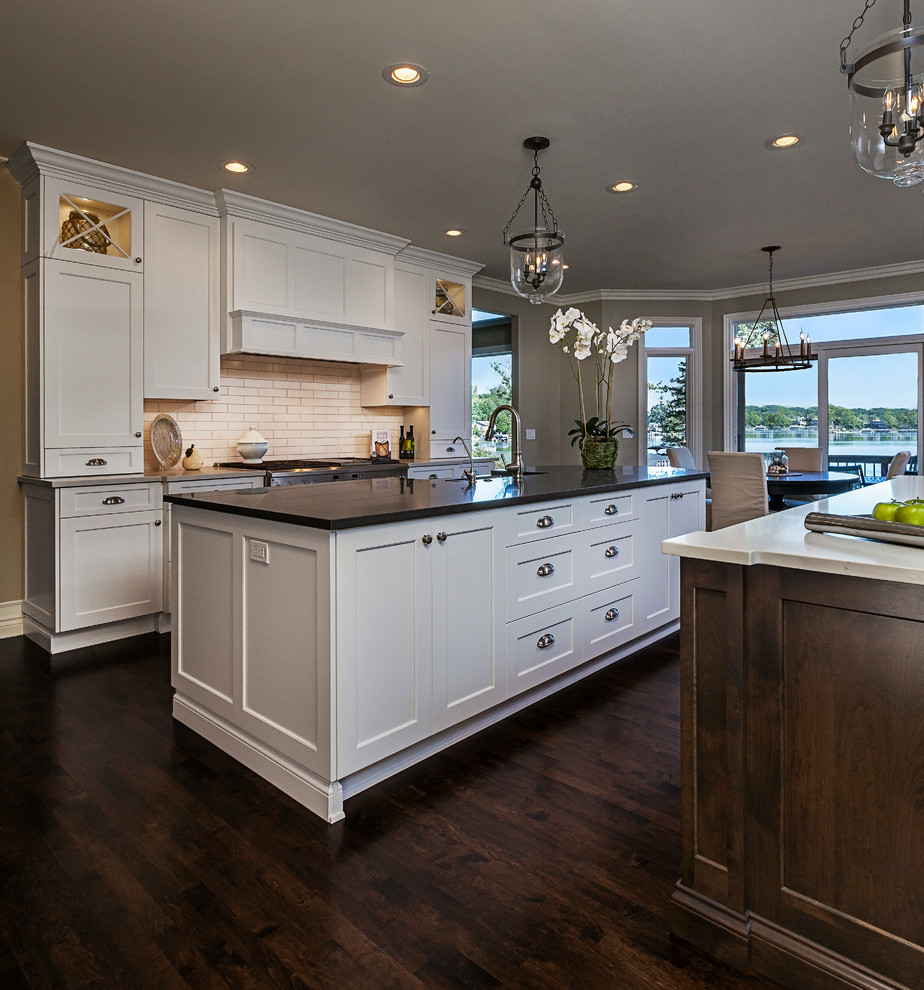 Eat-in kitchen - large transitional galley dark wood floor eat-in kitchen idea in Detroit with a farmhouse sink, shaker cabinets, white cabinets, quartz countertops, white backsplash, subway tile backsplash, stainless steel appliances and two islands