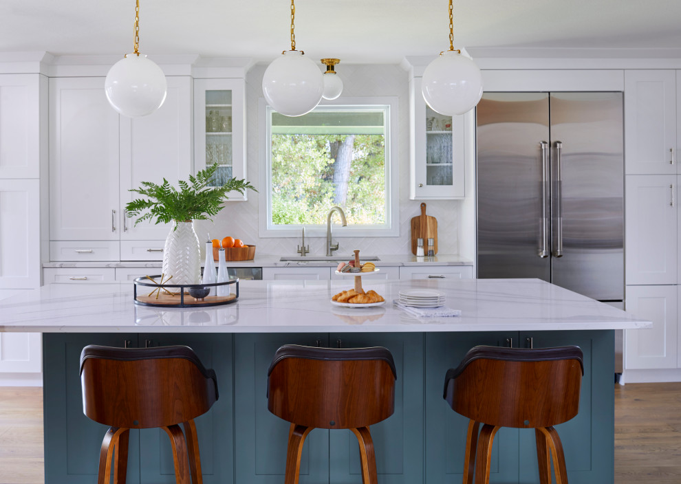 Mid-sized transitional l-shaped light wood floor and brown floor eat-in kitchen photo in Denver with a drop-in sink, recessed-panel cabinets, white cabinets, marble countertops, white backsplash, subway tile backsplash, stainless steel appliances, an island and multicolored countertops