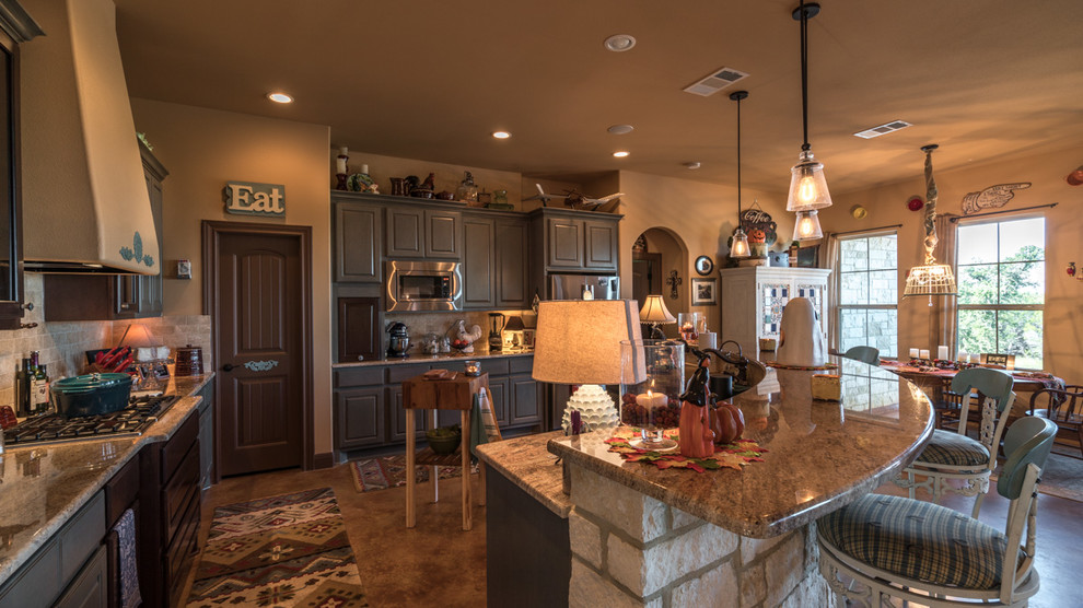 Example of a large mountain style l-shaped concrete floor eat-in kitchen design in Austin with shaker cabinets, an island, gray cabinets, granite countertops, beige backsplash, subway tile backsplash, stainless steel appliances and a farmhouse sink
