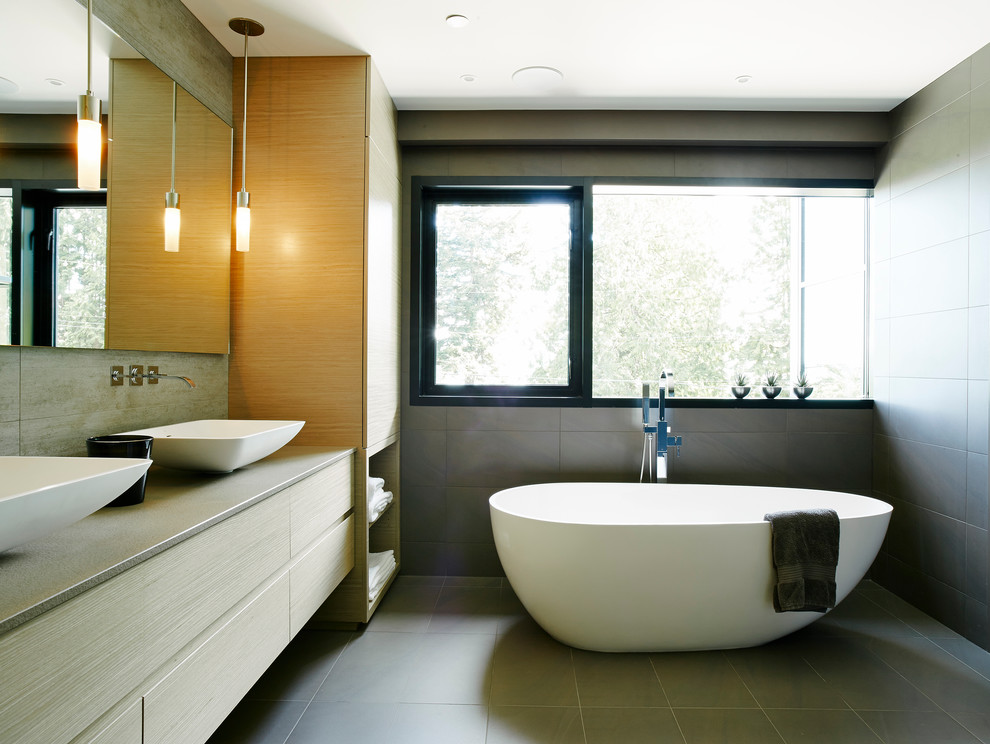 This is an example of a mid-sized contemporary master bathroom in Vancouver with a vessel sink, flat-panel cabinets, light wood cabinets, engineered quartz benchtops, a freestanding tub, an open shower, a wall-mount toilet, gray tile, porcelain tile, grey walls and porcelain floors.