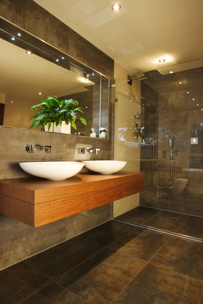 This is an example of a contemporary bathroom in Dorset with a vessel sink, wood benchtops, brown tile, a curbless shower, beige walls and brown benchtops.