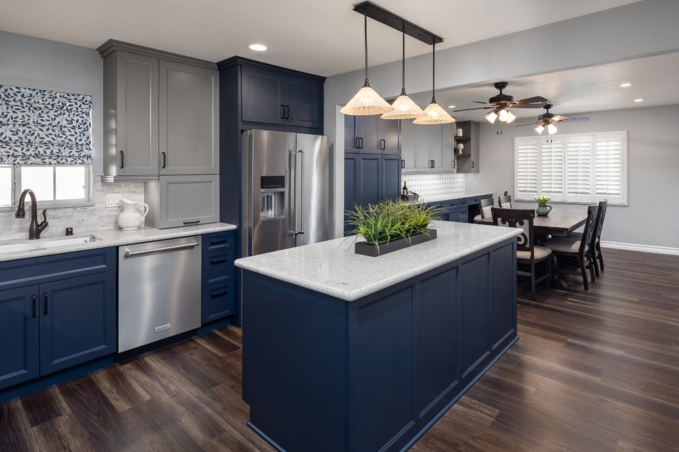 This is an example of a mid-sized country l-shaped eat-in kitchen in Orange County with an undermount sink, shaker cabinets, blue cabinets, quartz benchtops, grey splashback, limestone splashback, stainless steel appliances, vinyl floors, with island, brown floor and grey benchtop.
