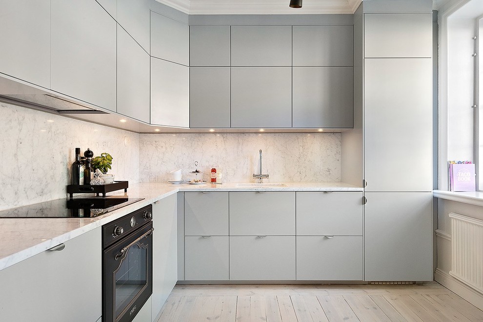 Inspiration for a mid-sized scandinavian l-shaped kitchen in Stockholm with a single-bowl sink, flat-panel cabinets, grey cabinets, white splashback, black appliances, light hardwood floors and no island.