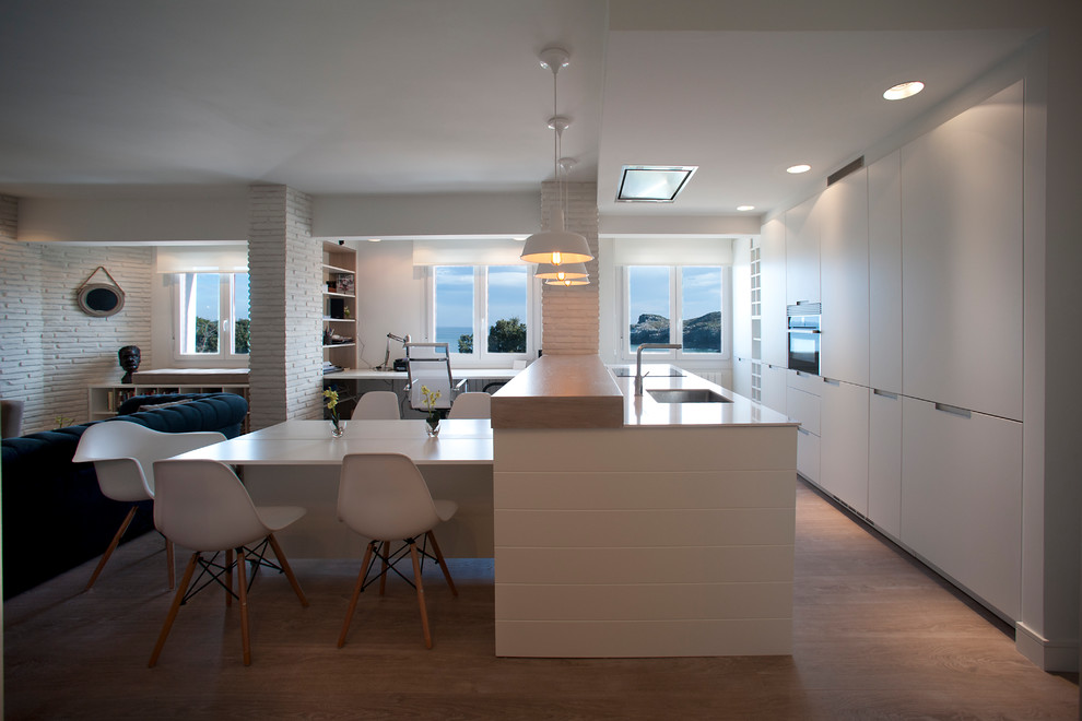 Mid-sized scandinavian galley open plan kitchen in Bilbao with an undermount sink, flat-panel cabinets, white cabinets, wood benchtops, stainless steel appliances, laminate floors, a peninsula and brown floor.