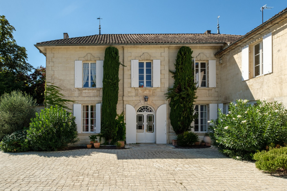 Photo of a large transitional two-storey yellow house exterior in Bordeaux with stone veneer, a hip roof, a tile roof and a red roof.