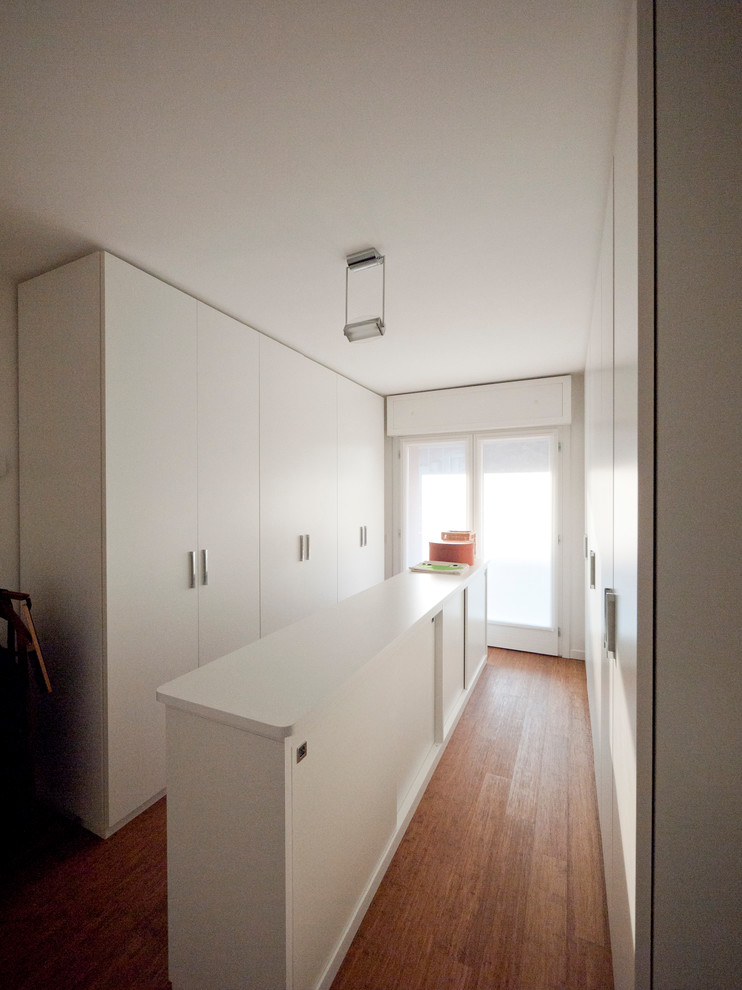 Photo of a large modern gender-neutral built-in wardrobe in Milan with flat-panel cabinets, white cabinets and bamboo floors.