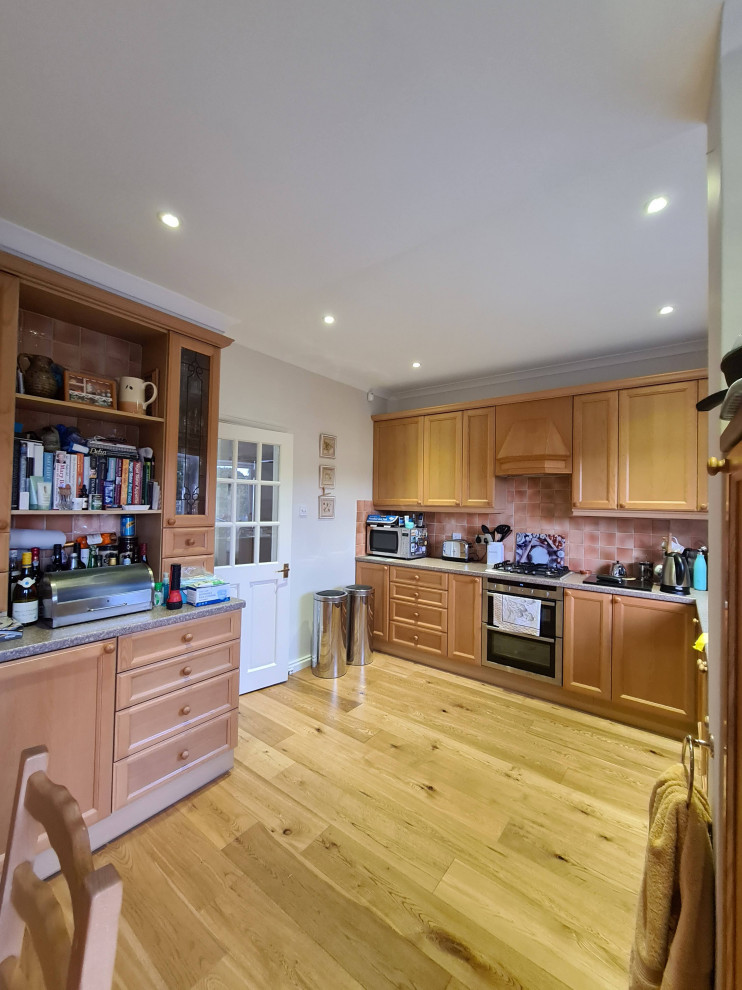 Large traditional l-shaped open plan kitchen in London with a drop-in sink, beaded inset cabinets, brown cabinets, granite benchtops, orange splashback, porcelain splashback, stainless steel appliances, light hardwood floors, no island, brown floor, grey benchtop and recessed.