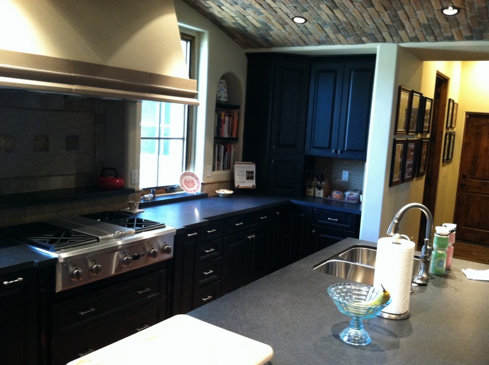 Example of a mid-sized transitional l-shaped light wood floor eat-in kitchen design in Phoenix with a double-bowl sink, raised-panel cabinets, black cabinets, solid surface countertops, gray backsplash, subway tile backsplash, stainless steel appliances and an island