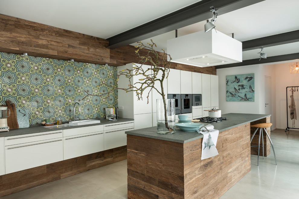 Design ideas for a large contemporary kitchen in Frankfurt with flat-panel cabinets, white cabinets, multi-coloured splashback, stainless steel appliances, with island, a drop-in sink, granite benchtops, ceramic splashback and concrete floors.