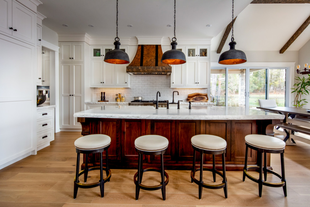 This is an example of a large country l-shaped eat-in kitchen in Toronto with a farmhouse sink, shaker cabinets, white cabinets, quartz benchtops, white splashback, subway tile splashback, panelled appliances, light hardwood floors, with island, beige floor and white benchtop.