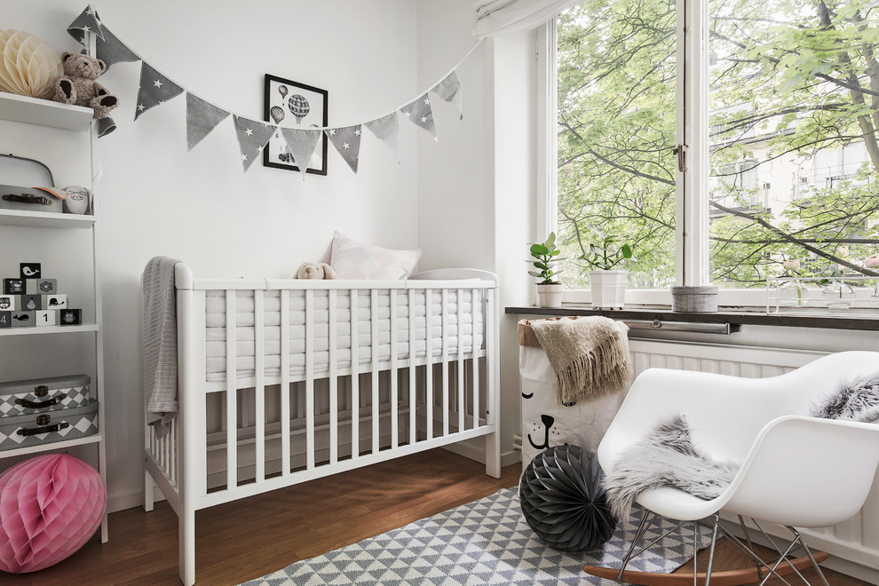 This is an example of a mid-sized scandinavian gender-neutral nursery in Stockholm with white walls, light hardwood floors and brown floor.