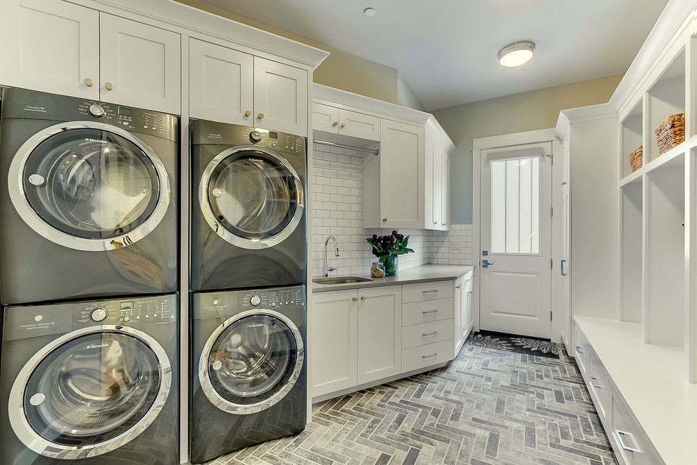 This is an example of a large traditional galley dedicated laundry room in Seattle with an undermount sink, shaker cabinets, white cabinets, grey walls, brick floors, grey floor, quartz benchtops and a stacked washer and dryer.