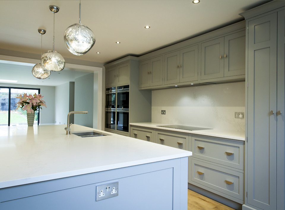 Inspiration for a mid-sized modern eat-in kitchen in London with an undermount sink, shaker cabinets, grey cabinets, solid surface benchtops, white splashback, stainless steel appliances, light hardwood floors, with island and white benchtop.